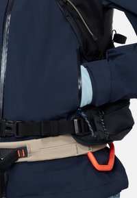 Posnetek osebe v mornarsko modri jakni, okoli pasu so varno pripeti črni in bež plezalni pasovi.