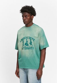 Grønne tie-dye oversized t-shirt med grafisk print af "CREATIVE DEPT" og "RETERNITY" i mørkegrøn. Korte ærmer og crew neckline.