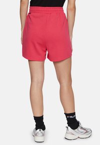 Pantalones cortos de mezcla de algodón rosa con cintura elástica, que presentan un diseño simple y una textura suave. Combinados con calcetines negros y zapatillas.