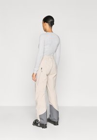 Beežid veekindlad suusapüksid hallide detailidega, millel on lukuga küljetaskud, lõdvestunud lõige ja tugevdatud ääred vastupidavuse tagamiseks.