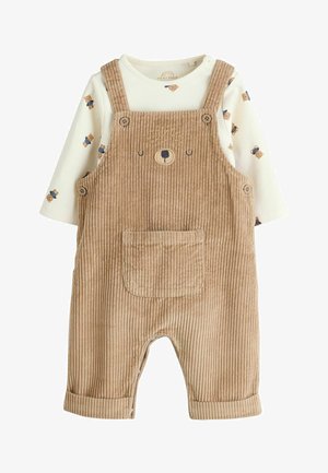 Peto de bebé de pana beige con cara de oso bordada en el bolsillo delantero, combinado con una camisa blanca de manga larga con estampado de pequeños ositos.