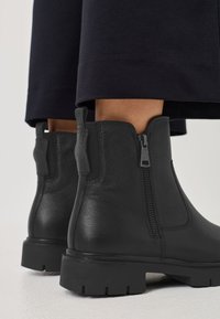 Schwarze Leder-Stiefeletten mit seitlichem Reißverschluss und strukturiertem Finish. Robuste Gummisohle. Sichtbare Nähte und Detail mit Zuglasche.