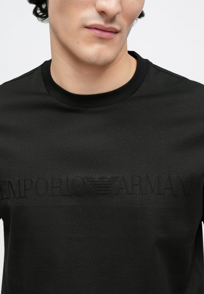 Μαύρο μπλουζάκι από λείο ύφασμα με στρογγυλή λαιμόκοψη, με ανάγλυφο λογότυπο "Emporio Armani" στο στήθος και διακριτική υφή.