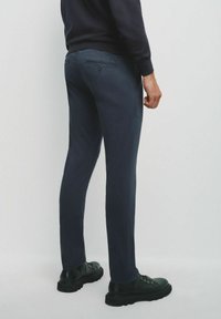 Granatowe spodnie o dopasowanym kroju, z tylną kieszenią i subtelną teksturą, zestawione z czarnymi sznurówkami.