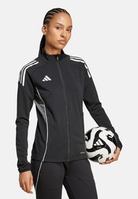 Schwarze Sportjacke mit weißen Streifen, hohem Kragen und Reißverschluss, kombiniert mit einem schwarz-weißen Fußball. Glatte Stofftextur.