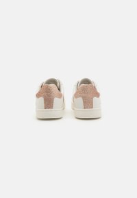 White sneakers featuring a textured pink glitter accent at the heel. Smooth leather material with a low-top design and rubber sole.