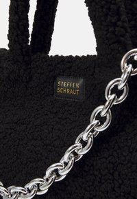 Czarna, pluszowa torba o teksturze z wysokiej jakości materiału z solidnymi uchwytami i błyszczący srebrny pasek. Zawiera czarną metkę z złotym napisem "STEFFEN SCHRAUT."