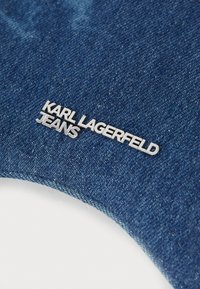 Denim-kangas, jossa on syvän sininen väri, ja jonka etupuolella on hopeinen metallilogo, jossa lukee "KARL LAGERFELD JEANS".