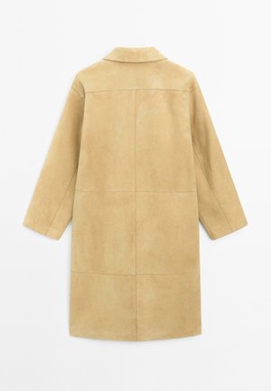 Manteau en suede beige avec un col, des manches longues et une coupe droite. Il présente des détails de couture avec une texture lisse sur un fond neutre.