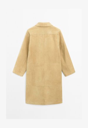 Manteau en suede beige avec un col, des manches longues et une coupe droite. Il présente des détails de couture avec une texture lisse sur un fond neutre.
