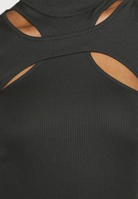 Top negro de canalé sin mangas con cuello alto, detalles recortados y aberturas en los costados. Textura suave con costura precisa.