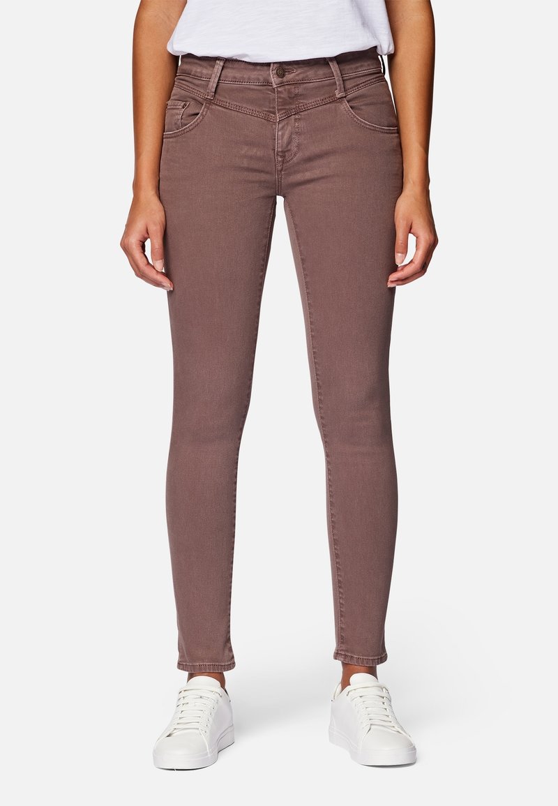 Jeans slim fit marrones de denim, con diseño de cinco bolsillos, pasadores para cinturón y detalles de costura, combinados con zapatillas blancas.