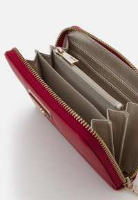 Rode leren portemonnee met gouden rits en accenten. Interieur met meerdere vakken en een ritsvak. Glad en textuur oppervlak.