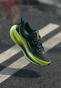 Nike løpesko med en mørkegrønn overdel, neongule aksenter og en polstret såle med en synlig luftenhet. Designet for komfort og ytelse.