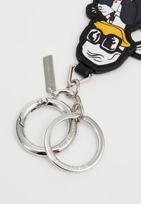 Black rubber keychain featuring a character with white and yellow accents, attached to two silver key rings. Notable brand tag visible.