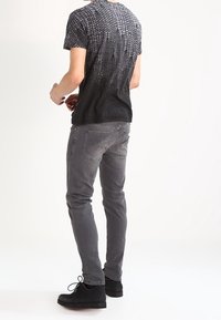 Svart och grå kortärmad t-shirt med ett gradient prickmönster, tillsammans med grå slim-fit jeans och svarta snörskor.