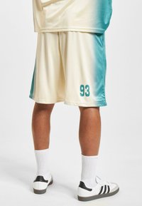 Ľahké basketbalové šortky v prechodnej béžovej až teal farbe. Na boku je vytlačené číslo "93" v teal farbe. Skombinované s bielymi topánkami a ponožkami.