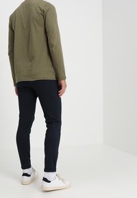 Långärmad olivgrön skjorta i kombination med åtsittande marinblå byxor, vita sneakers och vita strumpor med mörkblå detaljer. Enkelt mönster, avslappnad passform.