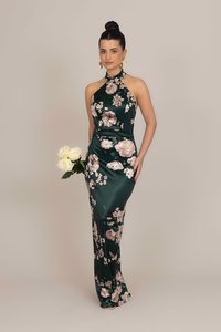 Langes grünes Satin-Kleid mit Halterneck und floralem Muster in Pink und Creme. Das Modell hält einen Strauß weißer Rosen.