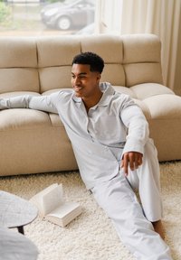 Ensemble de pyjama rayé à manches longues de couleur bleu clair et blanc, avec un col et une poche, porté en se prélassant sur un canapé beige avec un livre à proximité.