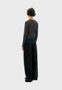 Zijdeachtige zwarte blouse met lange mouwen en horizontale strepen, gecombineerd met zwarte wijde broekspijpen. De stof is lichtgewicht en semi-transparant.