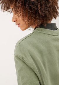Felpa verde oliva con scollatura rotonda e spalle scese, dotata di un colletto nero testurizzato sul retro e tessuto liscio.