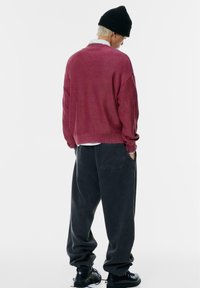 Maglione oversized color marsala con orlo e maniche a coste, abbinato a pantaloni grigi scuri a vestibilità ampia e stivali neri con lacci.
