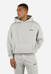 Lichtgrijze hoodie van zacht materiaal, met een voorzak en het "PEGADOR" logo op de borst in zwart. Ruime pasvorm met ribgebreide manchetten.