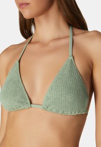 Mintgrön triangulär bikinioverdel gjord av texturerad tyg, med tunna remmar och veckade detaljer vid basen.