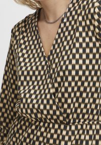 Mustakassi ja beež ruuduline kleit sügava V-kaelusega, kokku volditud vöökoha ja pikkade varrukatega. Sile kangas, millel on veidi tekstureeritud viimistlus.