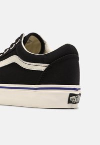 Czarne sneakersy na płaskiej podeszwie z białymi akcentami, z falistym paskiem po boku oraz gumową podeszwą z niebieskim i białym paskiem.