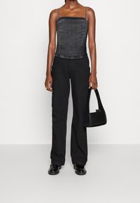Top in denim nero con corsetto e spalline sottili, abbinato a pantaloni neri a gamba dritta. Gli accessori includono una piccola borsa nera e scarpe lucide.