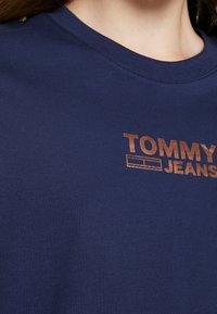 Námorně modré bavlněné tričko s bronzovým logem "TOMMY JEANS" na přední straně, klasickým kulatým výstřihem a jemnou texturou.