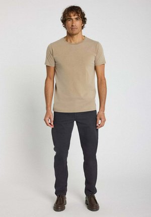 T-shirt beige à manches courtes associé à un pantalon gris foncé et des chaussures brunes, avec un design simple et une texture de tissu lisse.