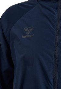 Giacca blu navy con cerniera frontale e un logo hummel discreto sul petto sinistro.