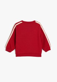 Felpa rossa con scollatura a girocollo, vestibilità rilassata e cuciture centrali. Strisce laterali beige e polsini a costine aggiungono texture e dettaglio.