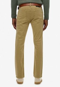 Pantalones de algodón color beige claro con un diseño de pierna recta, cuatro bolsillos y detalles de costura sutiles. La tela tiene una textura suave.