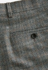Grau karierte Hosen aus strukturiertem Stoff, ausgestattet mit einem Knopf und einer kleinen Tasche. Das Muster enthält braune und hellere graue Elemente.
