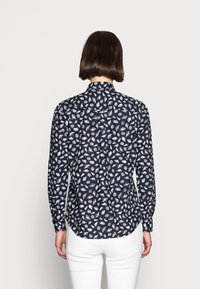Blusa navy a maniche lunghe con motivo a foglie bianche, colletto e polsini. Vestibilità slim con orlo curvo e dettaglio con bottoni sul retro.