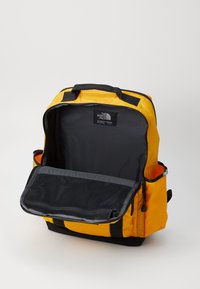 Gul og sort rygsæk med struktureret design, topgreb og en frontlomme i mesh. Åbent indre med mørk foring.