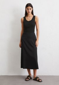 Top negro sin mangas con detalle de botones, combinado con una falda larga negra fluida y sandalias negras con un broche dorado. Textura suave.