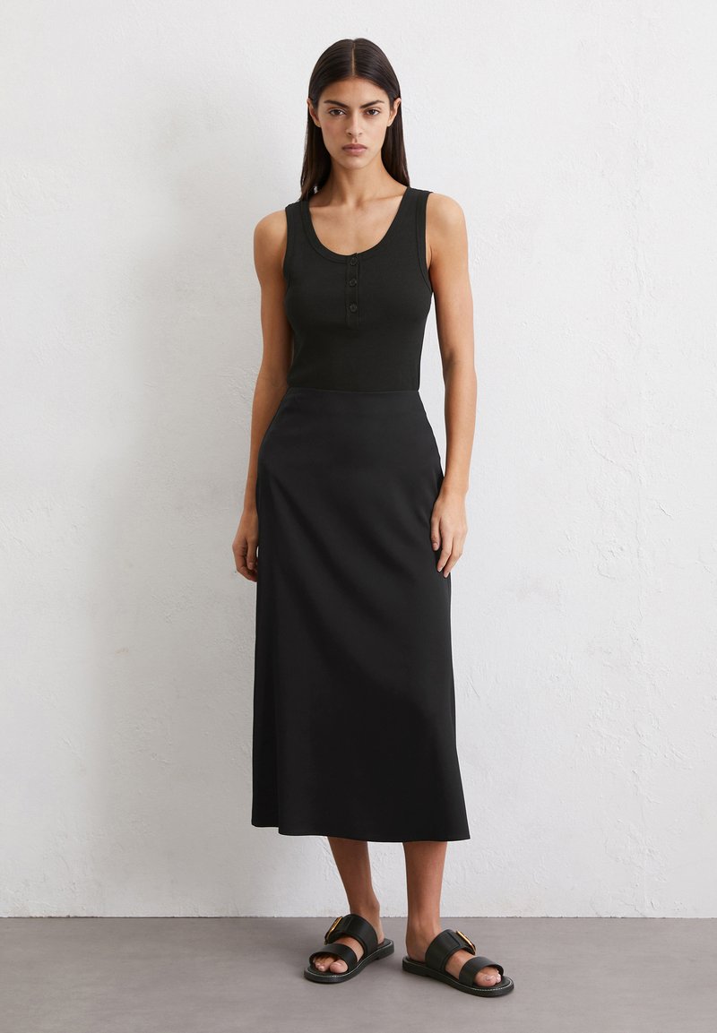Top negro sin mangas con detalle de botones, combinado con una falda larga negra fluida y sandalias negras con un broche dorado. Textura suave.