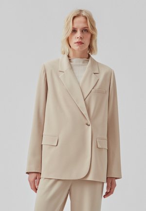 Beige damesblazer lavet af glat stof, med en spids revers, enkeltknaplukning og to forlommer.