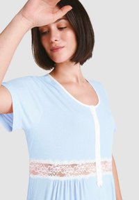 Camisón azul claro hecho de una tela suave, con un frente blanco abotonado y un delicado encaje en la cintura. Mangas cortas.