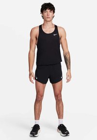 Débardeur sportif sans manches noir et shorts avec le logo Nike blanc, associés à des baskets noires et des chaussettes blanches à la cheville. Texture de tissu lisse.