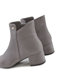 Gray suede ankle boots with a block heel, featuring an angular design and a small metal accent on the side. Smooth textured finish.