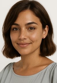 Guldfågel studörhängen, delikat design, rena linjer; bärs av en person med medelbrunt hår, slät hy och naturlig sminkning mot en ljus bakgrund.