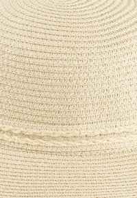 Szeroki kapelusz z plecionych naturalnych włókien, o teksturowanym kremowym kolorze, wyposażony w plecioną opaskę wokół dolnej części.