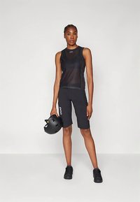Ensemble débardeur et short de sport noirs, fabriqués en tissu respirant. Le mannequin tient un casque noir, renforçant l'esthétique sportive.