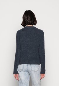 Pull en tricot gris foncé, doté d'un col rond, de manches longues et d'une coupe légèrement raccourcie. Texture douce, avec un motif côtelé.